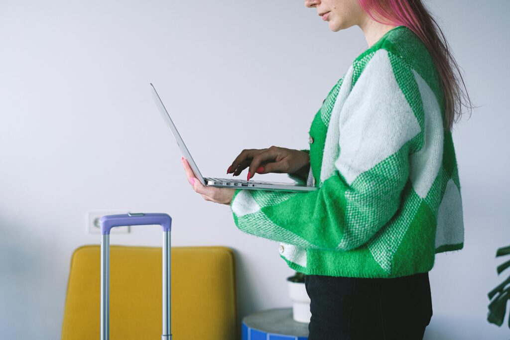 Young woman working on laptop near luggage in stylish hotel lounge, embracing the digital nomad lifestyle.
